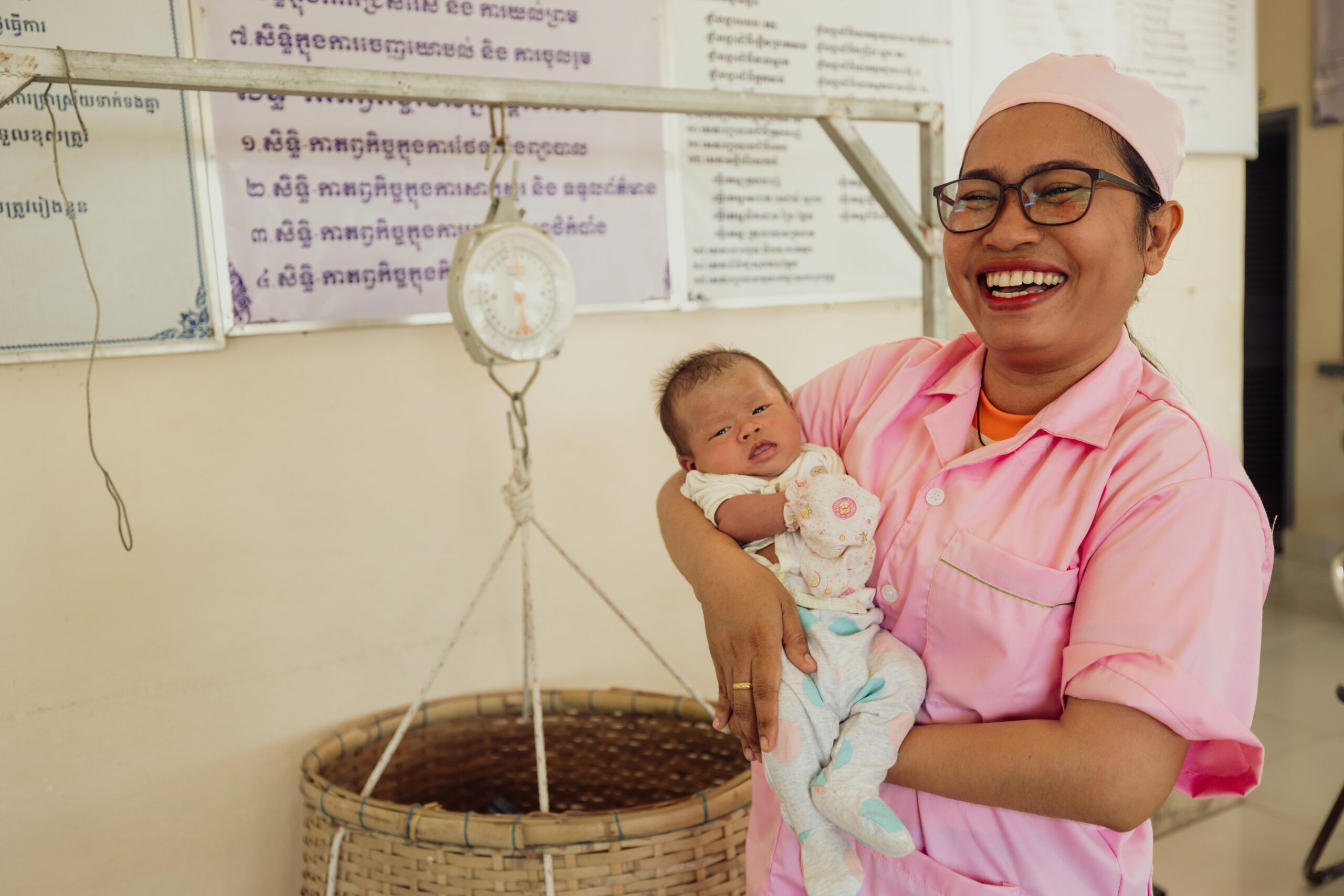 Vannak from Cambodia, dressed in pink medical scrubs, holds a baby.